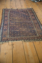 Antique Belouch rug corner with navy, brown geometric wave border, and worn ends.
