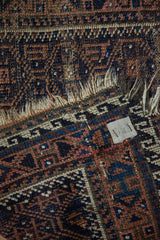 Antique Belouch rug end detail with tattered fringe and worn navy, brown geometric pattern.