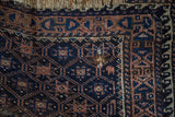Antique Belouch rug corner detail with geometric trellis, visible small hole, and tattered fringe.