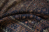 Folded antique Belouch rug shows navy, coffee brown geometric starbursts and textured pile.