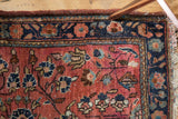 Vintage Sarouk rug corner with dusty raspberry floral field, navy border, and tattered fringe.