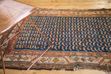 Antique Hamadan rug: navy mahi-mahi field, saffron geometric border, and aged, tattered edge.