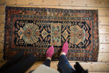 Corner of a vintage Persian Hamadan rug with navy, madder root rust, and sky blue stylized floral patterns.