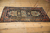 Vintage Hamadan rug corner shows navy, rust, sky blue floral motifs, low pile, tattered fringe.