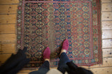 Antique West Persian rug's corner, showing red, blue, saffron patterns, worn fringe.