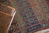 Antique West Persian rug's worn hand-knotted pile, showing repeating floral medallions and tattered edge.
