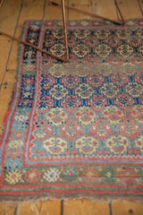 Antique West Persian rug corner detail: madder red border, repeating panel medallions, visible end tatter.