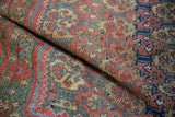 Folded antique West Persian rug revealing hand-knotted pile, madder red, navy, and saffron floral motifs.