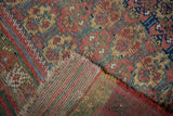 Antique West Persian rug's tattered end, worn pile, and striped foundation.