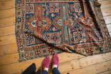 Antique Caucasian rug corner, geometric boteh motifs in madder, navy, saffron, and tattered edge.