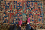 Antique Caucasian rug with bold geometric cross motif, repeating boteh in navy, red, and saffron.