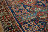 Geometric boteh motifs in navy, madder red, and saffron on an antique hand-knotted Caucasian rug showing wear.