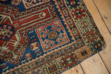 Antique Caucasian rug corner with tattered edges, showing geometric patterns and foundation.