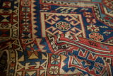 Geometric boteh motifs in navy, madder red, and saffron on a folded Antique Caucasian rug.