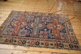 Antique Caucasian rug corner detail: geometric navy, madder red, saffron patterns, and wear.