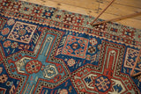 Close-up on antique Caucasian rug's geometric motifs with navy, madder red, and saffron colors.