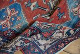 Folded vintage Malayer rug section displaying geometric red, blue, ivory patterns, low pile.