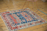 Antique Serapi rug corner showcasing asymmetric red, navy, ivory borders, with tattered edge.