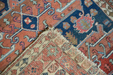 Antique Serapi rug corner revealing red and navy pile, hand knotted foundation, tattered fringe.