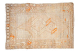 Hand-knotted distressed Oushak rug with faded gul medallions, neutral tones, and tangerine orange accents.