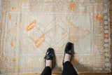 Vintage distressed Oushak rug's ivory and sand field with tangerine geometric motifs and even wear.