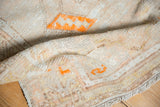 Distressed Oushak rug texture with tangerine orange motifs, faint foundation showing, and fringe.