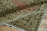 Distressed low pile of a curled antique Tabriz rug, showing dusty pink and brown motifs.