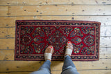 Corner of vintage Persian Sarouk rug, cherry red floral field, navy border, intact selvage.