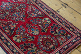 Vintage Sarouk rug corner, cherry red field, floral sprays, ornate border, and side selvage.
