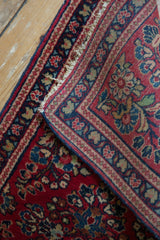 Folded vintage Sarouk rug: cherry red floral pile, navy border, and woven reverse.