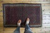 Antique Belouch rug showcasing geometric diamond patterns, wine red and navy hues, with aged pile and tattered edges.