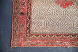 Worn corner of an antique Persian Malayer rug showing red vine borders, lattice field, and edge loss.