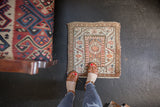 Feet on vintage Malayer square rug mat, revealing its low pile and paneled medallion pattern.