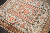Vintage Malayer rug's paneled medallions, pawn border, and vine motifs in soft ivory and rose tones.