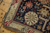 Antique Caucasian rug corner with geometric animal motifs, madder red, and tattered sand fringe.