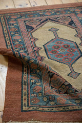 A folded corner on an antique camel hair Serab rug reveals its hand-knotted texture and intact raspberry border.