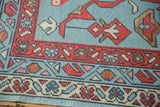 Oushak rug corner close-up: faded denim blue field, madder red, ivory borders, vine and boteh.