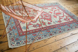 Oushak rug corner: madder red boteh, faded blue vine borders, and ivory field blossoms.