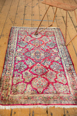 Corner of vintage Sarouk rug showing raspberry field, intricate floral border, and ivory fringe.