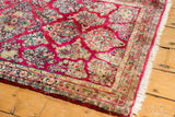 Corner of vintage Sarouk runner with intricate floral border, raspberry field, and white fringe.