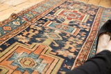 Close-up of antique Karaja runner's primitive geometric motifs in navy, red, and orange, showing wear.