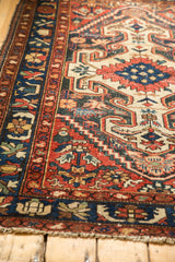 Baktiari rug corner with navy floral border, red field, and light tattered fringe.