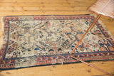 Distressed corner of antique Shirvan rug, showing red-blue borders, ivory field, and tattered fringe.