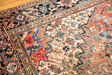 Detail of vintage Heriz carpet with geometric patterns, time-softened brick red, navy, and ivory hues. Faint foundation visible.