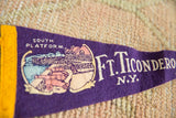 Detail of vintage purple felt pennant showing 'Ft. Ticonderoga N.Y.' text and cannon art.