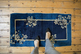 Antique Peking rug corner: indigo blue field, beige double border, floral sprays, low pile.