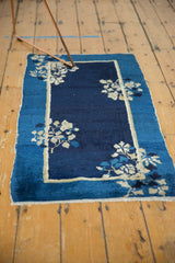 Antique Peking rug corner showing indigo blue field, beige floral spray, and low pile texture.