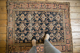 Dark navy geometric floral gul motif, pale blush meandering border, with visible wear and tattered edge.