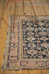 Antique Caucasian rug corner; pale blush border with geometric vine, navy field with gul motifs, and worn edges.