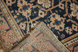Folded antique Caucasian rug corner: dark navy geometric pile, tattered edges, and hand-knotted foundation.